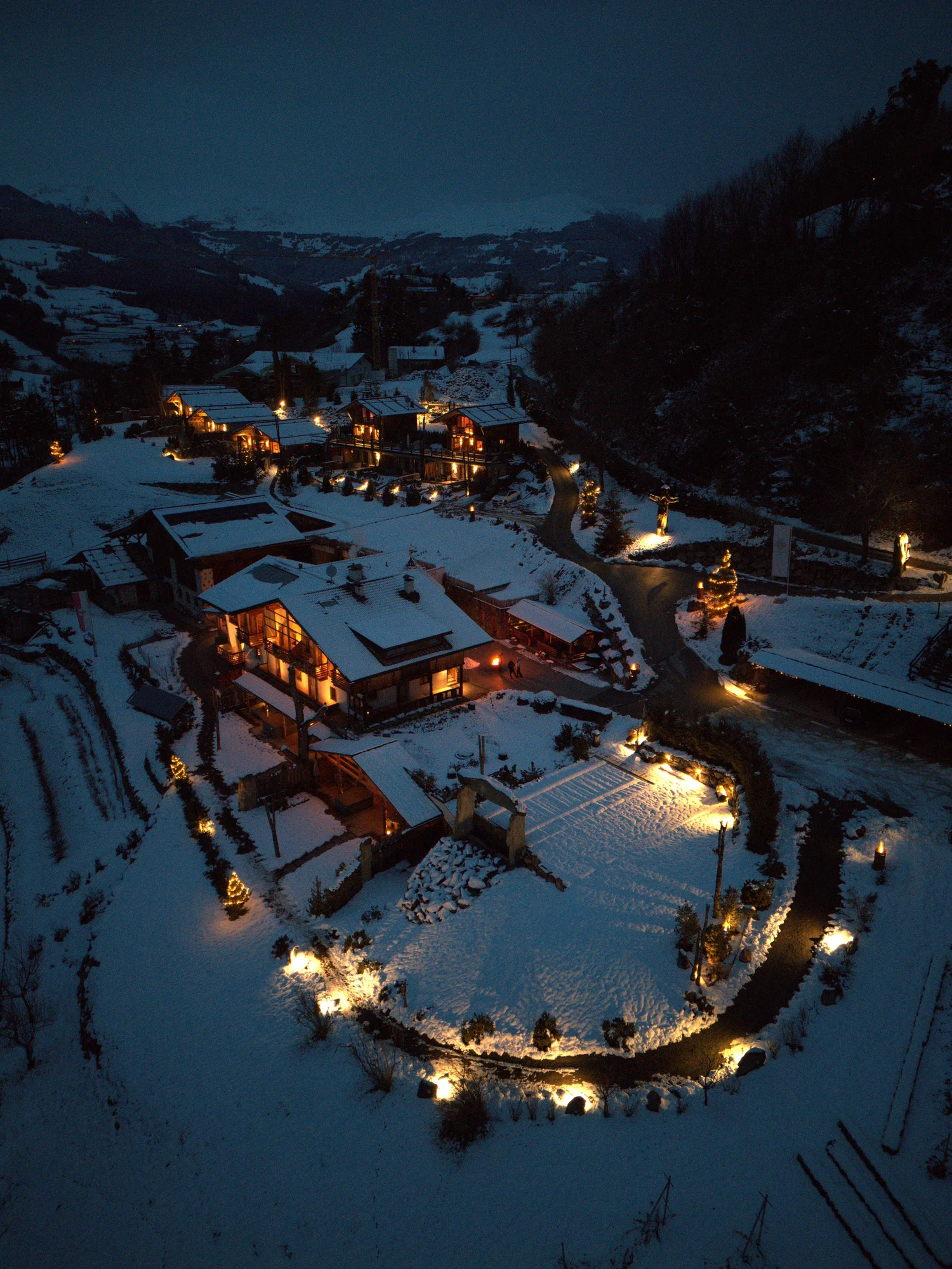 A winter drone photograph of the warmly lit Kirchwies Resort chalets in the snow
